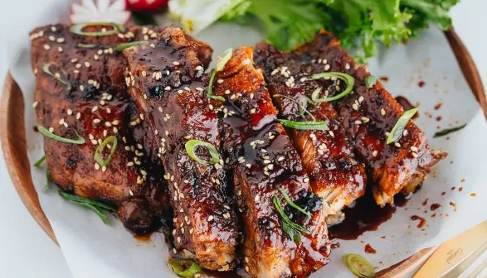A platter of tender, caramelized Chinese sweet sticky ribs garnished with sesame seeds.