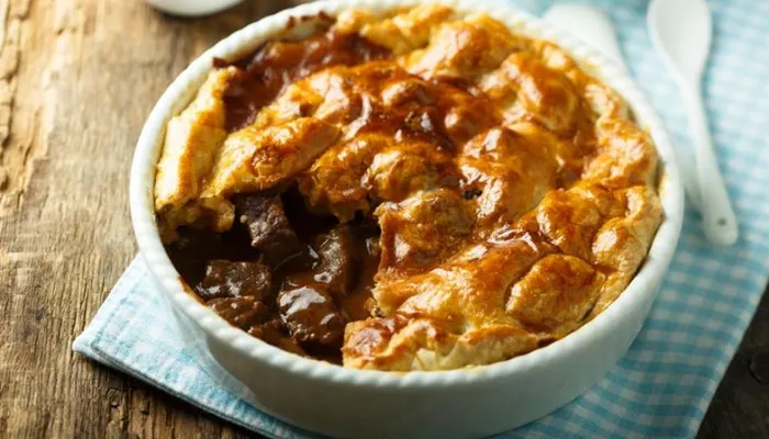 Close-up of a freshly baked, golden-brown steak and ale pie with rich gravy.