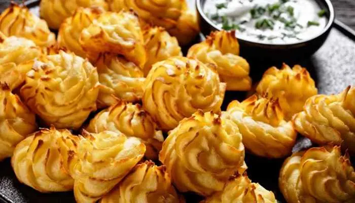 Elegant, golden-brown piped Duchess potatoes arranged on a white ceramic serving platter.